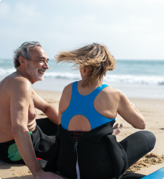 Man and woman sat on beach in wetsuits
